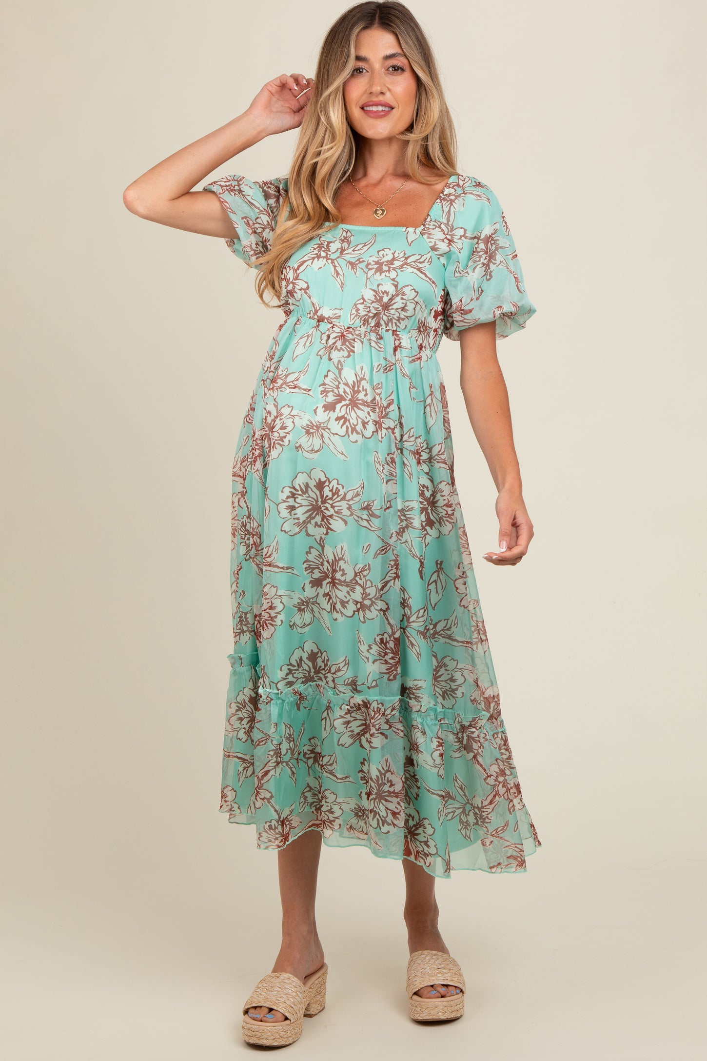 woman wearing a mint green floral maternity dress with short sleeves and a tiered skirt, showing her baby bump