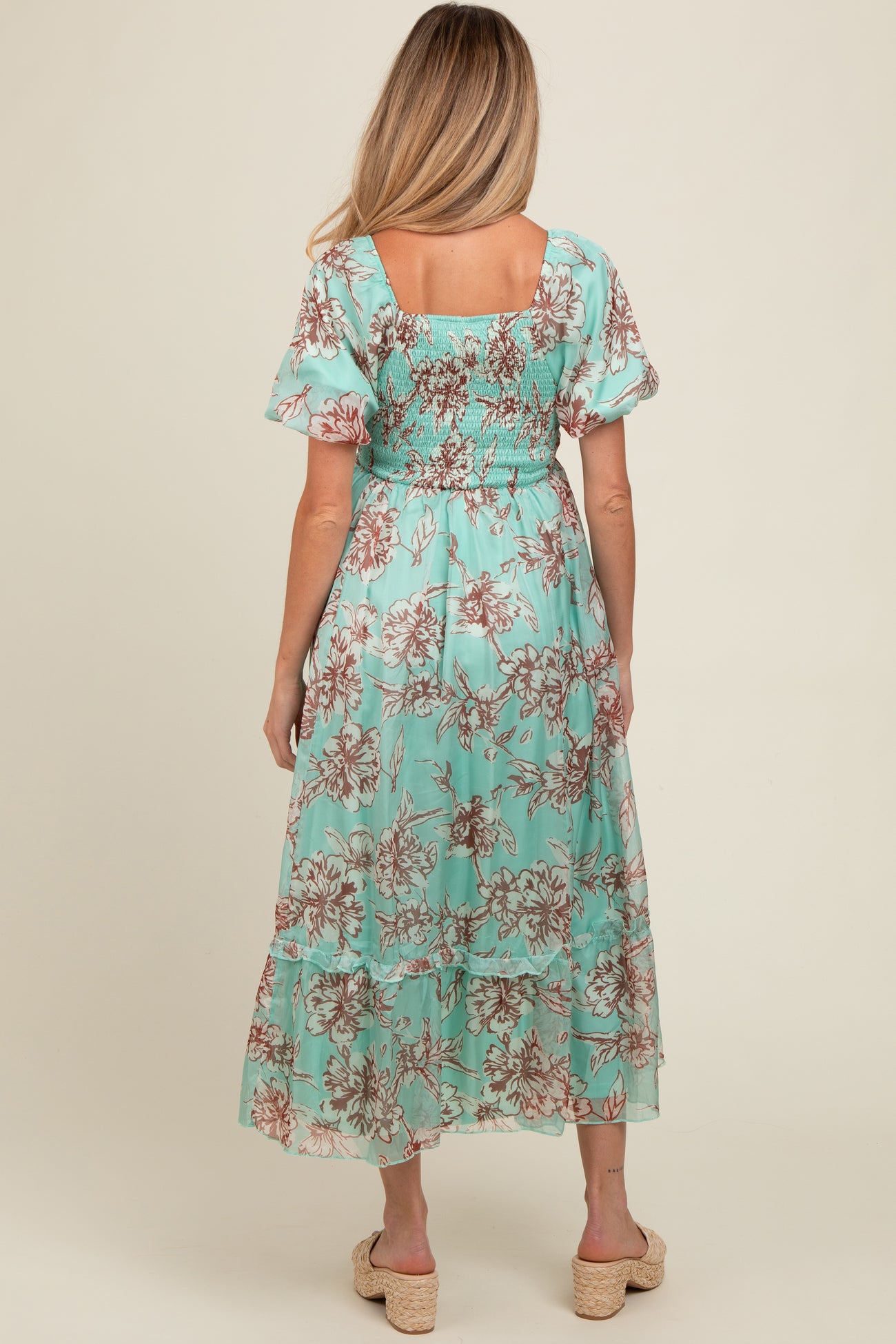 woman wearing a mint green floral maternity maxi dress with a smocked bodice and flutter sleeves, seen from the back