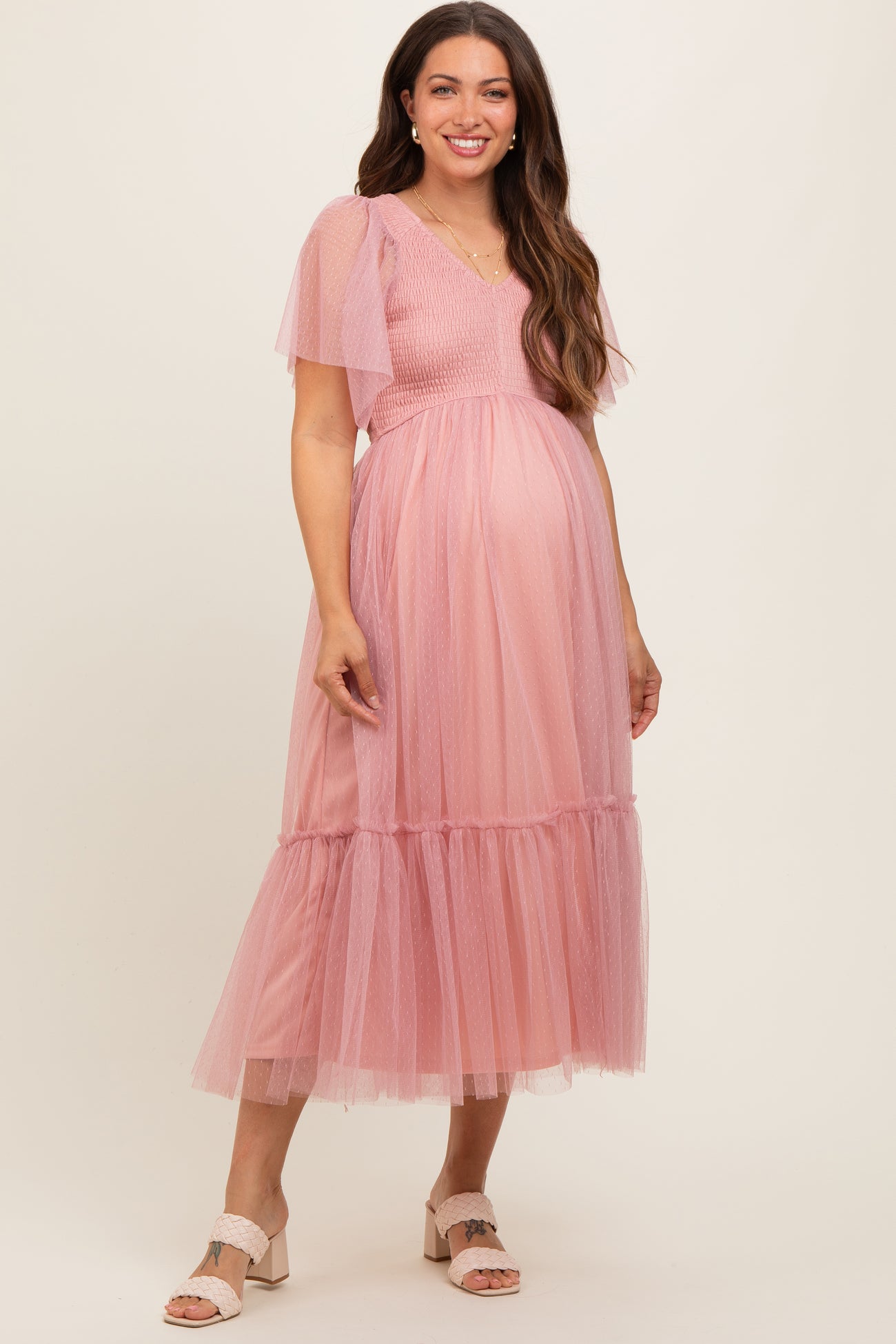 woman wearing a pink maternity dress with puff sleeves and a tiered tulle skirt, displaying her baby bump