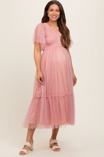 woman wearing a pink maternity dress with puff sleeves and a tiered tulle skirt, displaying her baby bump