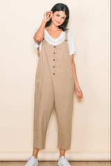 woman wearing a beige linen jumpsuit with buttons and side pockets over a white t-shirt and white sneakers