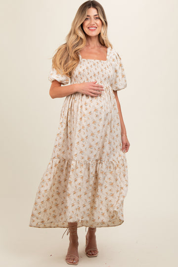 woman wearing a white floral maternity maxi dress with puff sleeves and a square neckline, gently holding her baby bump