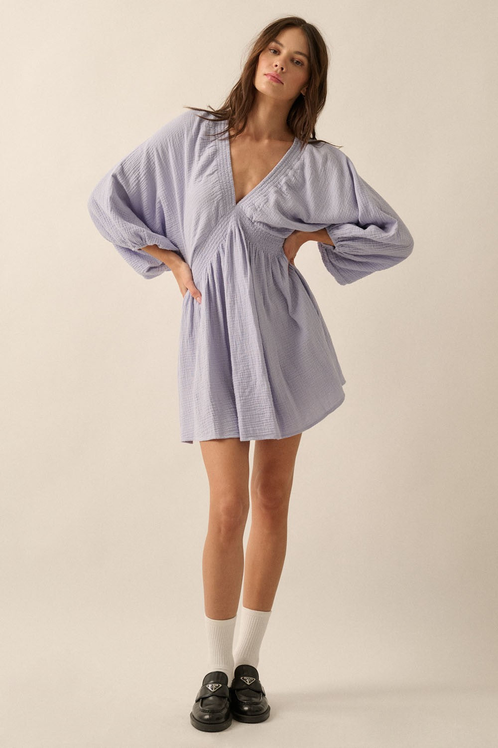 woman wearing a lavender short dress with billowy sleeves and a deep v-neckline, paired with black slip-on shoes