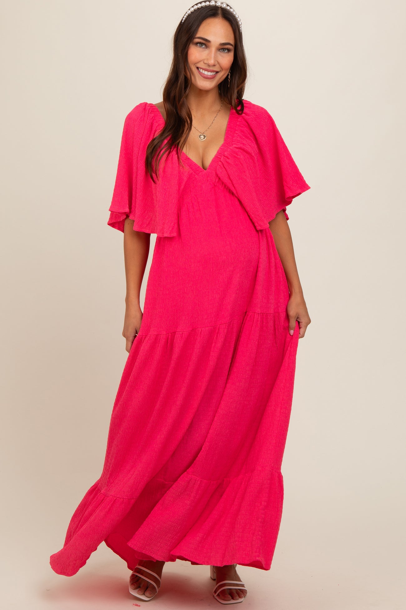 woman wearing a bright pink maternity maxi dress with flutter sleeves and a flowy skirt, showing her baby bump