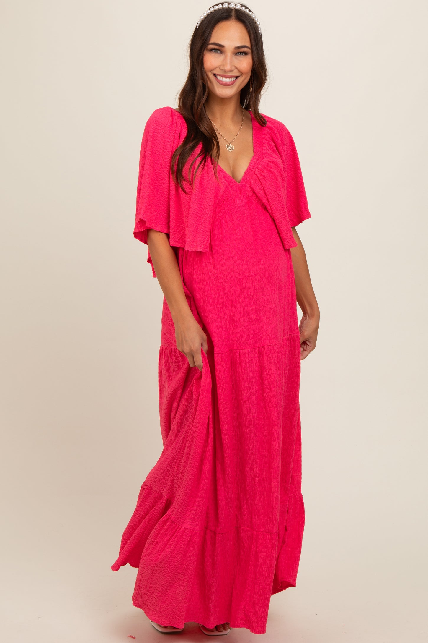 woman wearing a bright pink maternity maxi dress with a matching lightweight cardigan and a visible baby bump