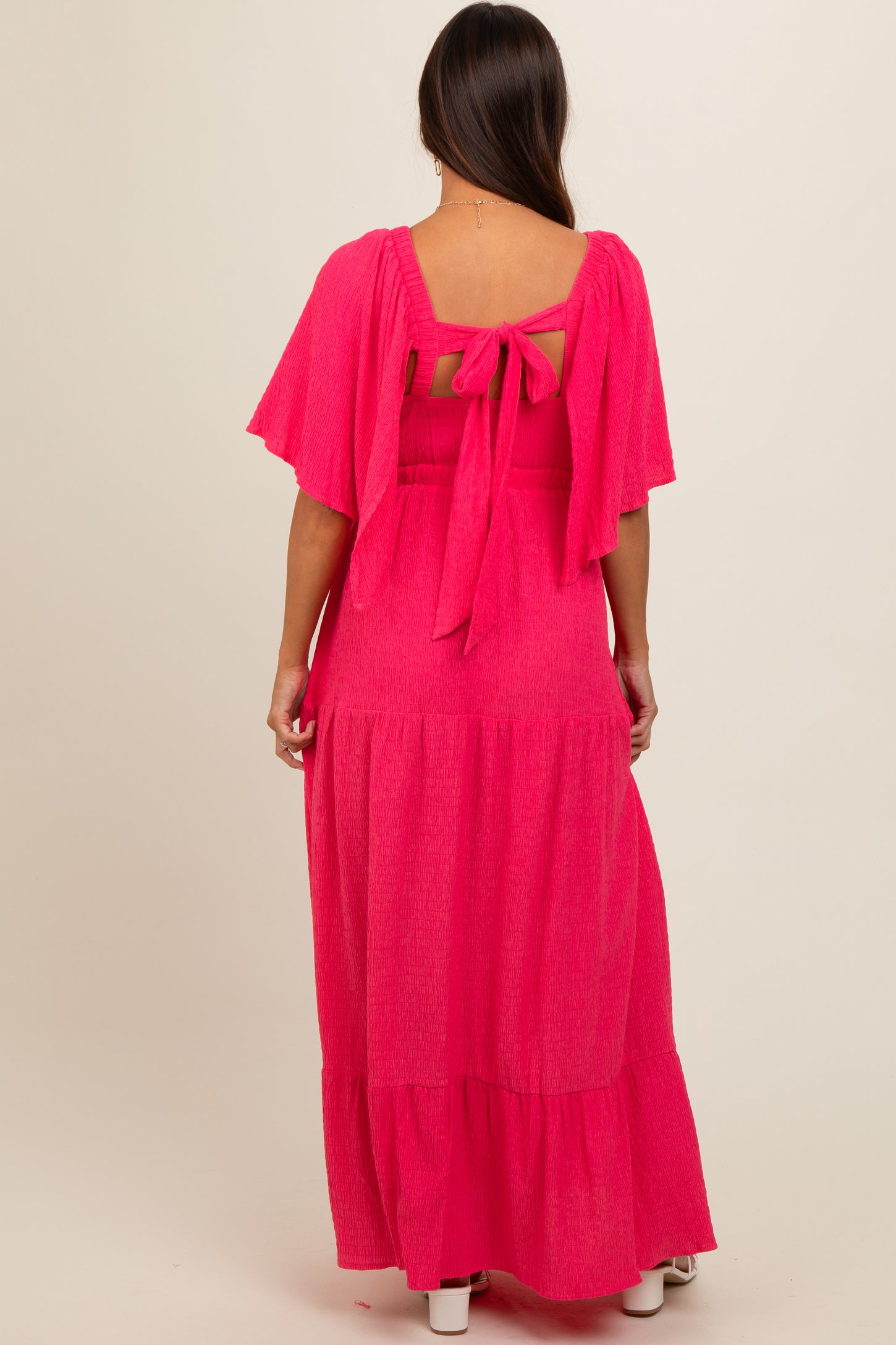 woman wearing a vibrant pink maternity maxi dress with flutter sleeves and a tie-back detail