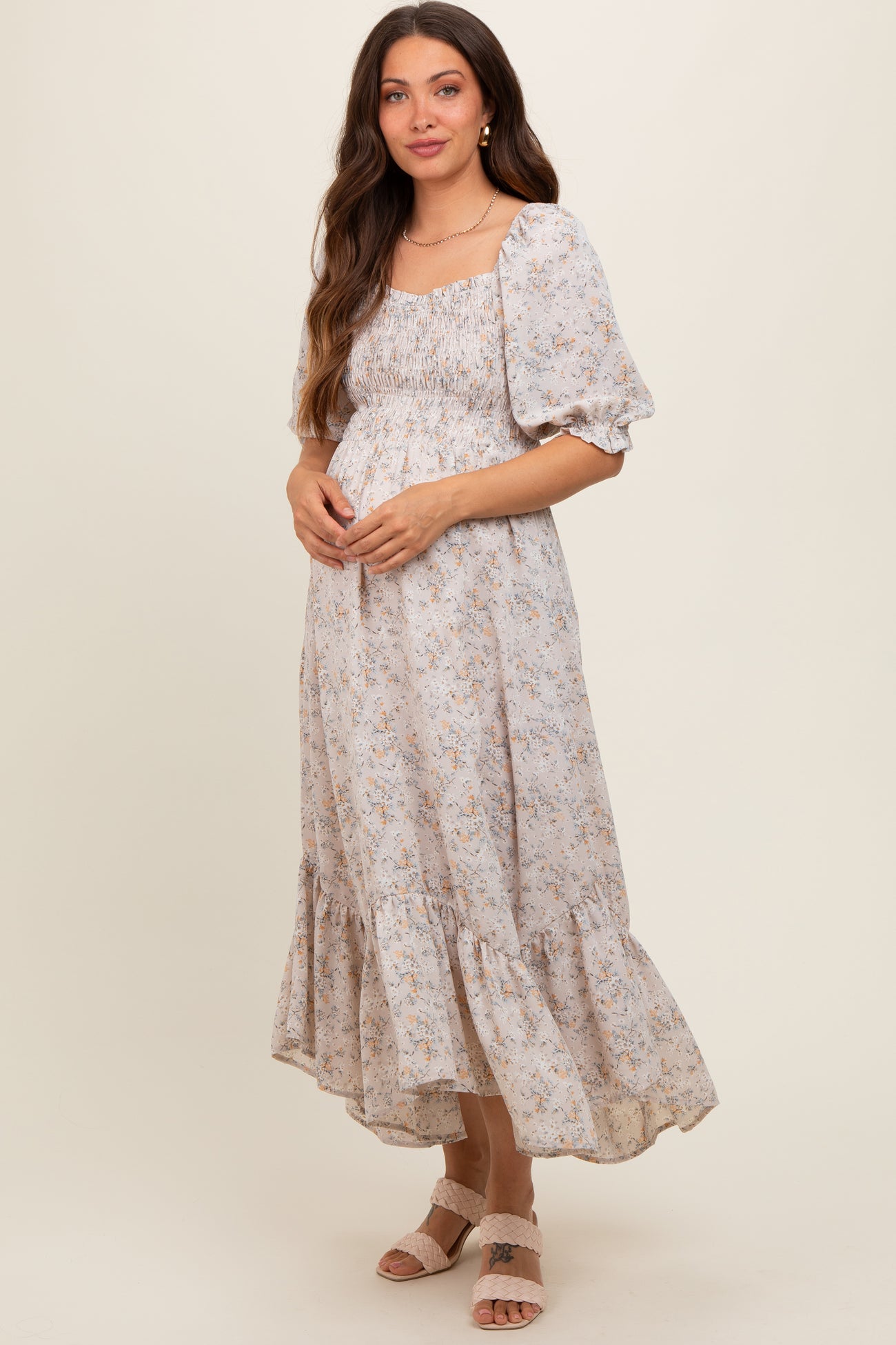 woman wearing a light floral print maternity dress with puff sleeves and a flowing hem, showing her baby bump
