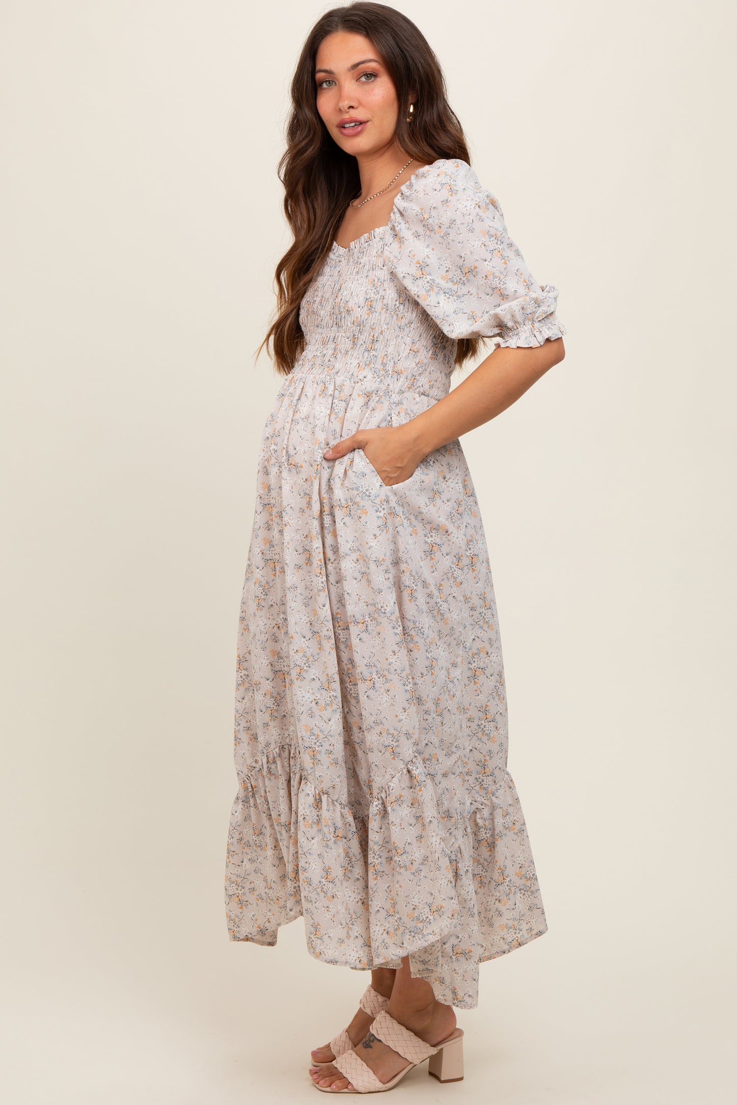 woman wearing a light floral maternity dress with puff sleeves and pockets, showcasing her baby bump