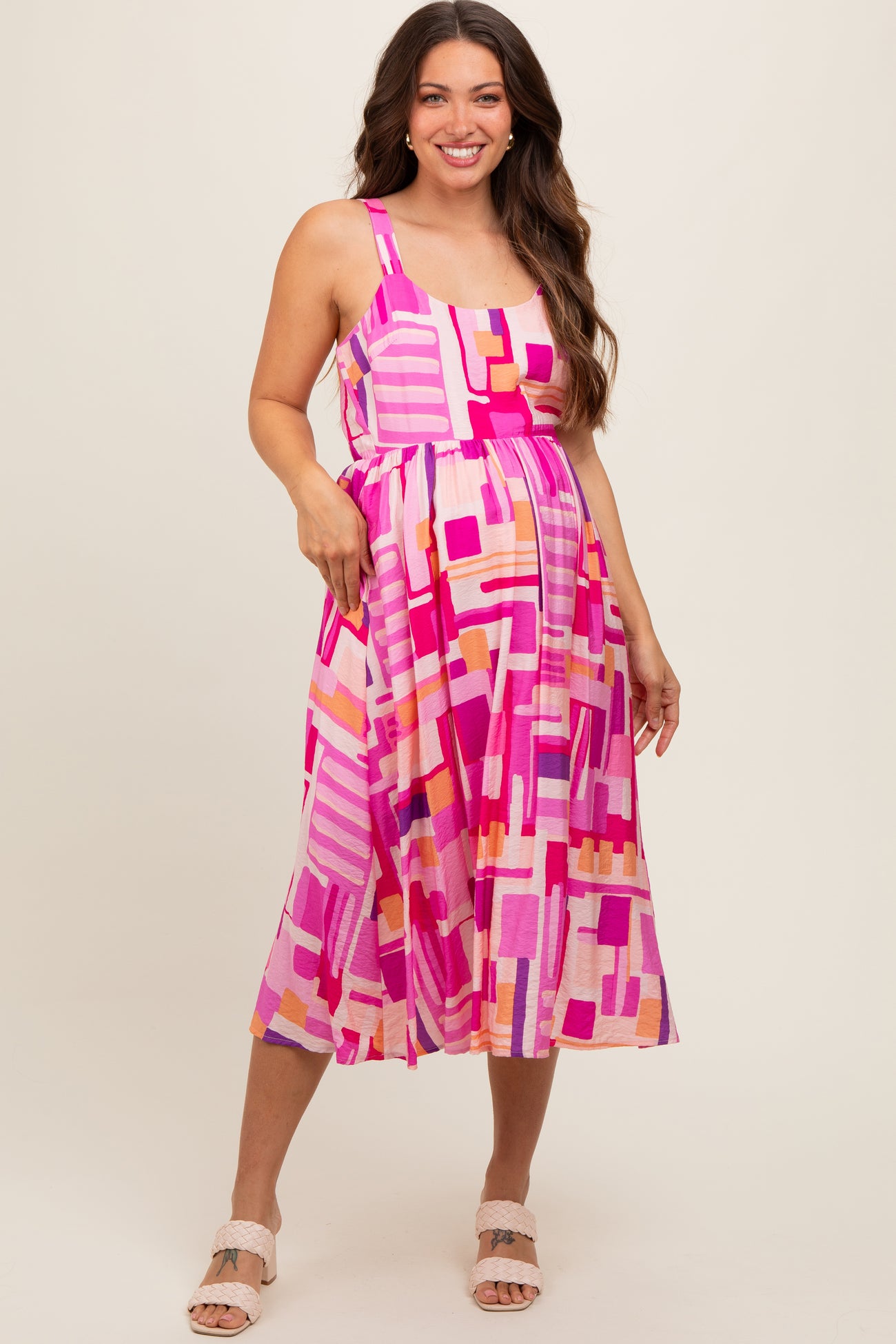 woman wearing a pink and multicolor abstract print maternity dress with a fitted bodice and flowy skirt, showing her baby bump