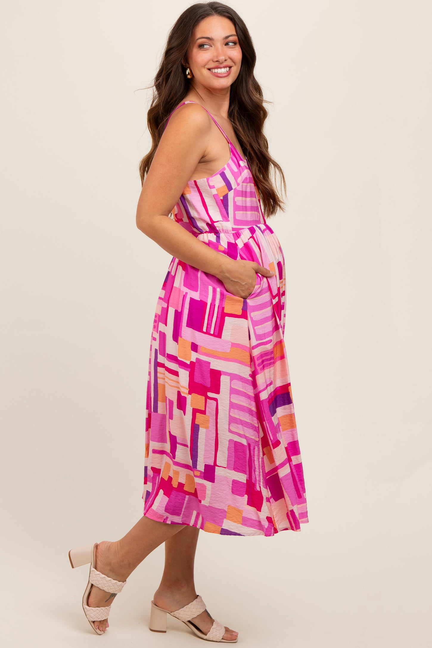 woman wearing a pink and multicolor patterned maternity dress with pockets and a visible baby bump