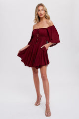 woman wearing a burgundy off-the-shoulder dress with bell sleeves and a skater silhouette, featuring a decorative button detail and pockets