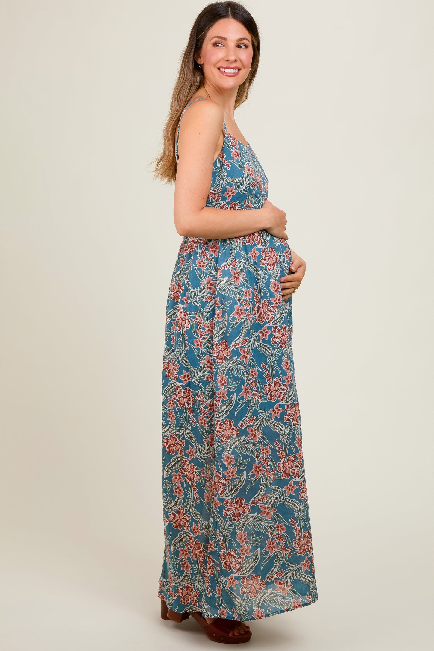 woman wearing a floral print maternity maxi dress, holding her baby bump and smiling