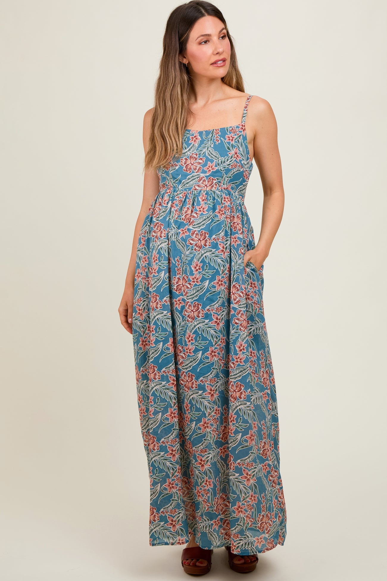 woman wearing a floral patterned blue maternity maxi dress with adjustable straps and pockets, baby bump visible