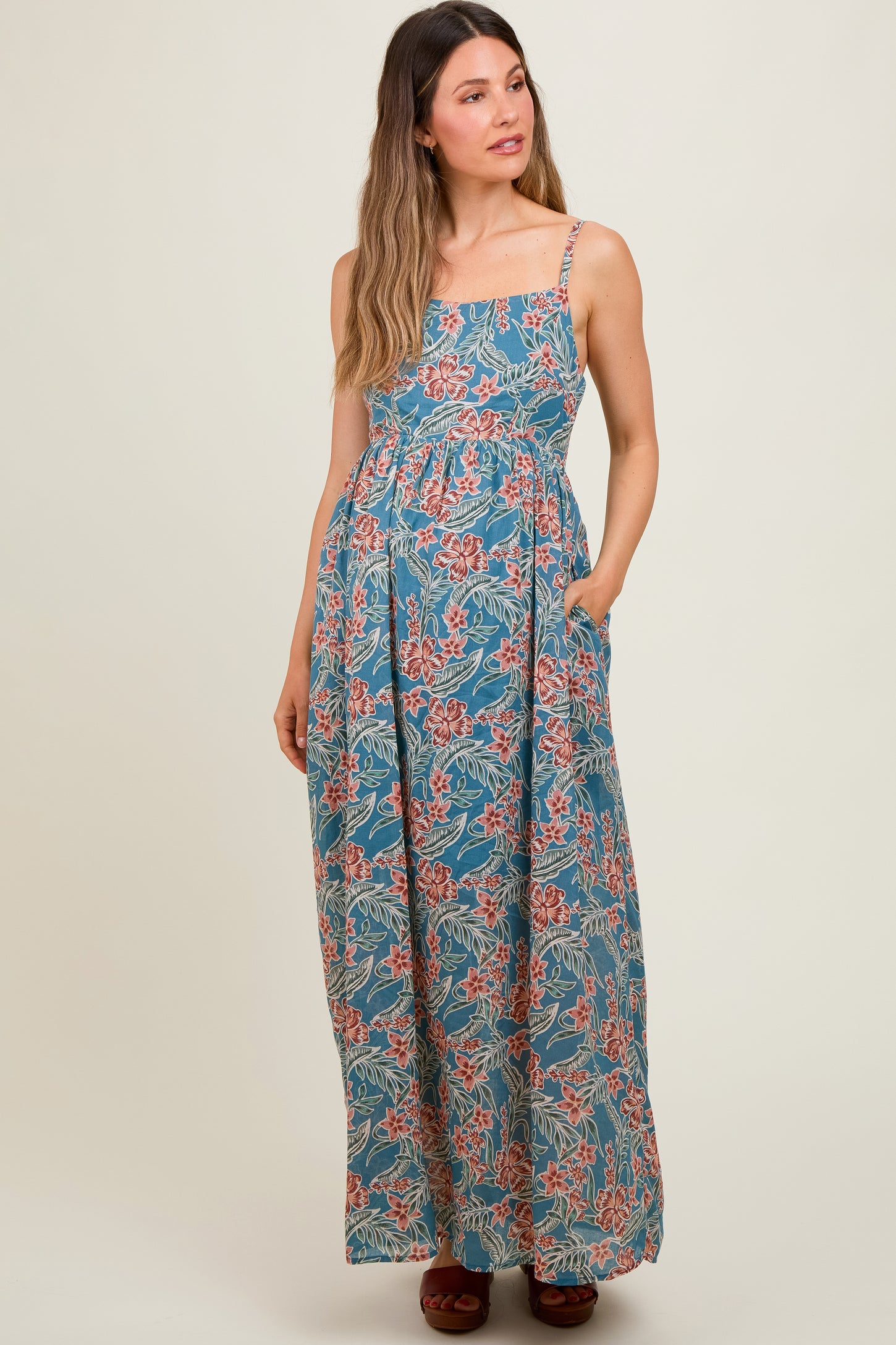 woman wearing a floral patterned blue maternity maxi dress with adjustable straps and pockets, baby bump visible