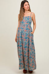 woman wearing a floral patterned blue maternity maxi dress with adjustable straps and pockets, baby bump visible