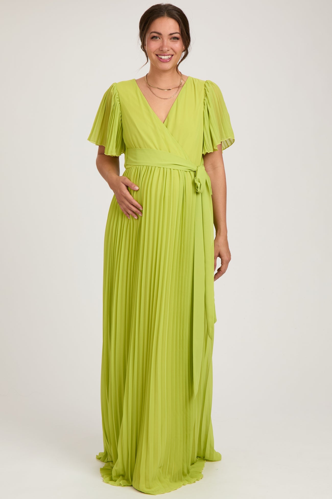woman wearing a lime green pleated maternity wrap dress with short flutter sleeves and a tie waist, displaying her baby bump