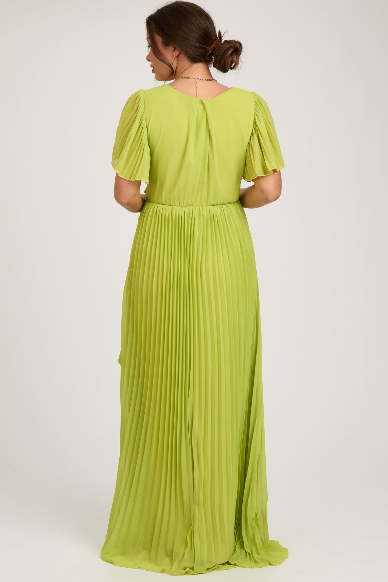 woman wearing a pleated lime green maternity maxi dress with short puff sleeves and a tie waist detail, seen from the back