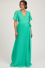 woman wearing a green pleated maternity maxi dress with short flutter sleeves and a tie waist, showing her baby bump