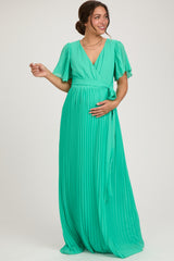woman wearing a green pleated maternity dress with short flutter sleeves, gently cradling her baby bump