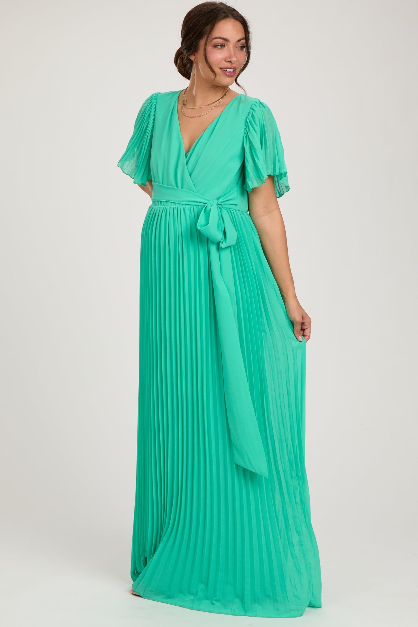 woman wearing a flowing pleated mint green maternity dress with short flutter sleeves and a tie waist, showcasing her baby bump