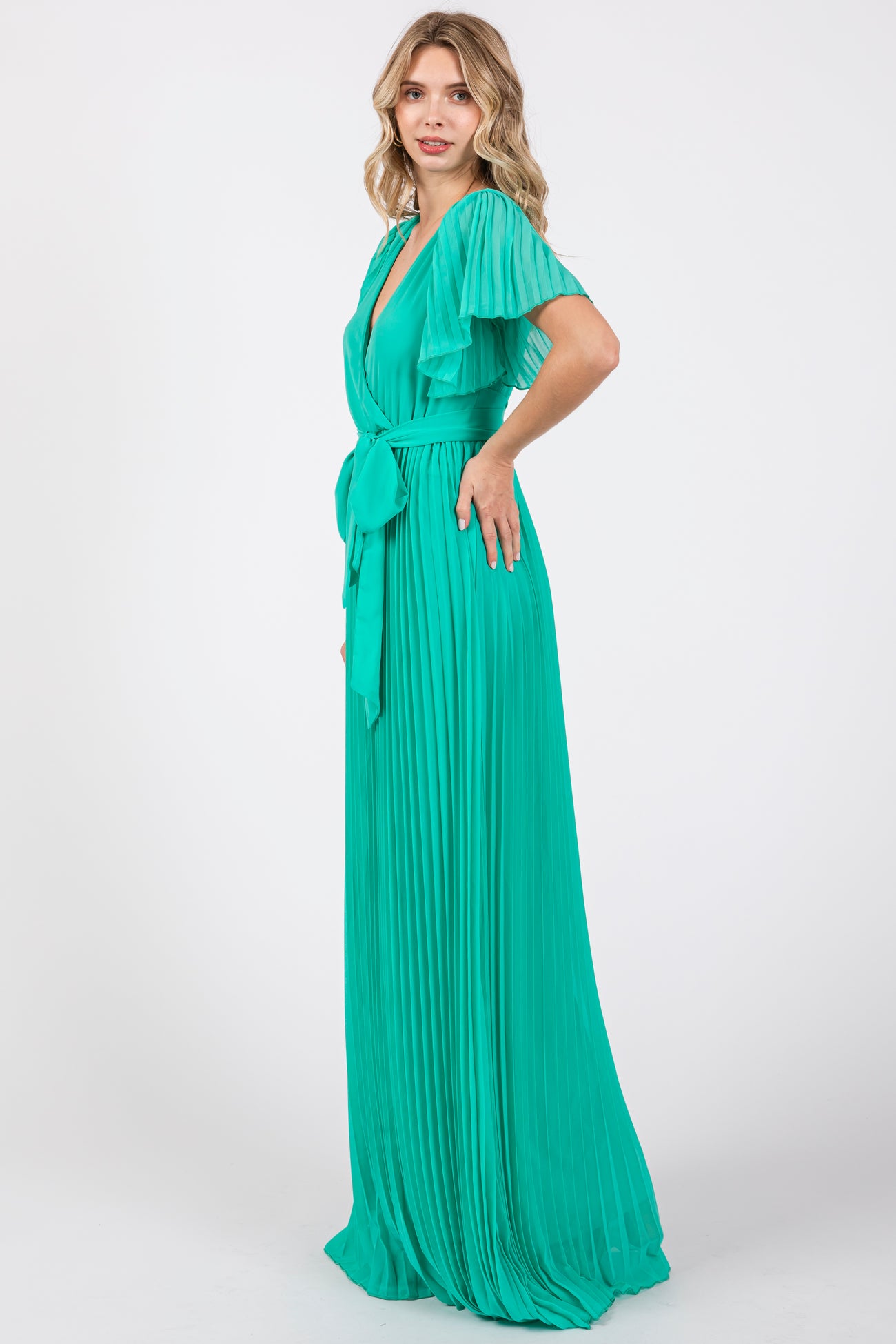 woman wearing a long mint green pleated gown with flutter sleeves and a tie waist detail