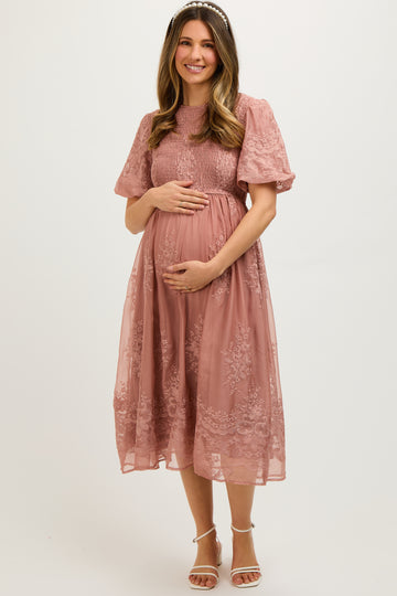 woman wearing a dusty rose maternity dress with short puff sleeves and lace details, cradling her baby bump