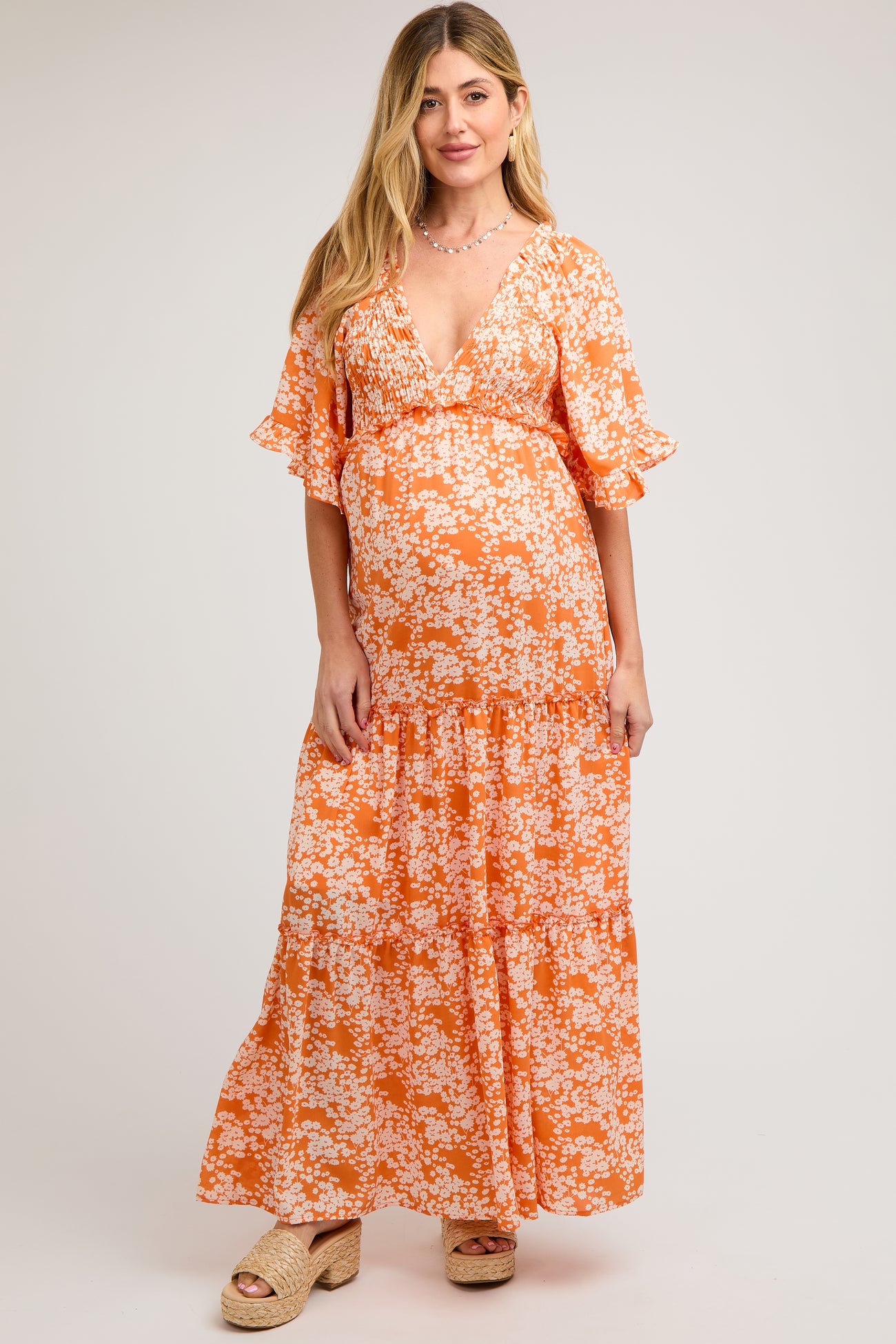 woman wearing a floral orange maternity maxi dress with a deep v-neckline and ruffled sleeves, showing her baby bump