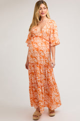 woman wearing a floral orange maternity maxi dress with a v-neckline and ruffled sleeves, showcasing her baby bump