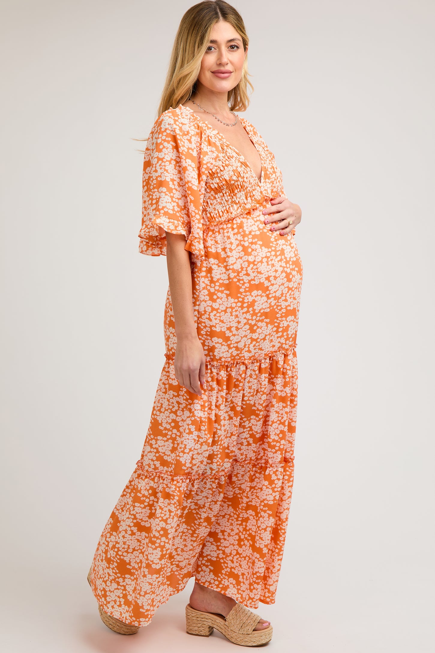 woman wearing an orange floral maternity maxi dress and holding her baby bump