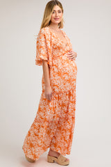 woman wearing an orange floral maternity maxi dress and holding her baby bump