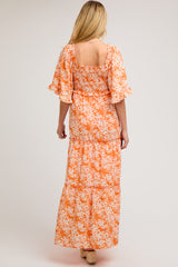 woman wearing an orange floral maternity maxi dress with flutter sleeves and a smocked bodice, showing off her baby bump