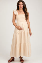 woman wearing a beige maternity maxi dress with ruffled straps and a smocked bodice, holding her baby bump