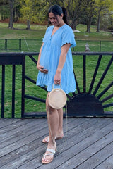 woman wearing a light blue maternity dress with flutter sleeves and a baby bump, holding a round woven bag