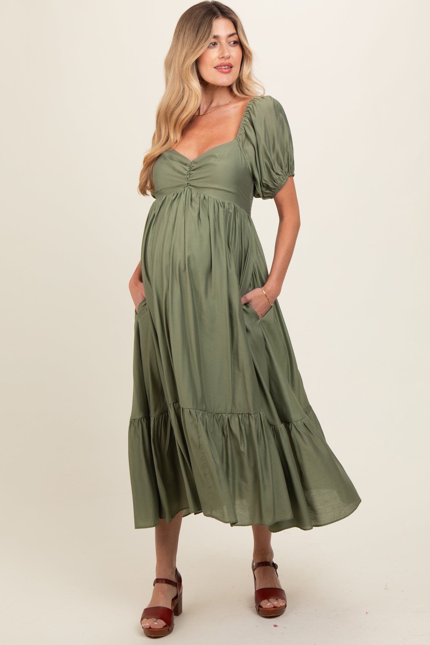 woman wearing a green puff sleeve maternity dress with a tiered skirt and pockets, showing her baby bump