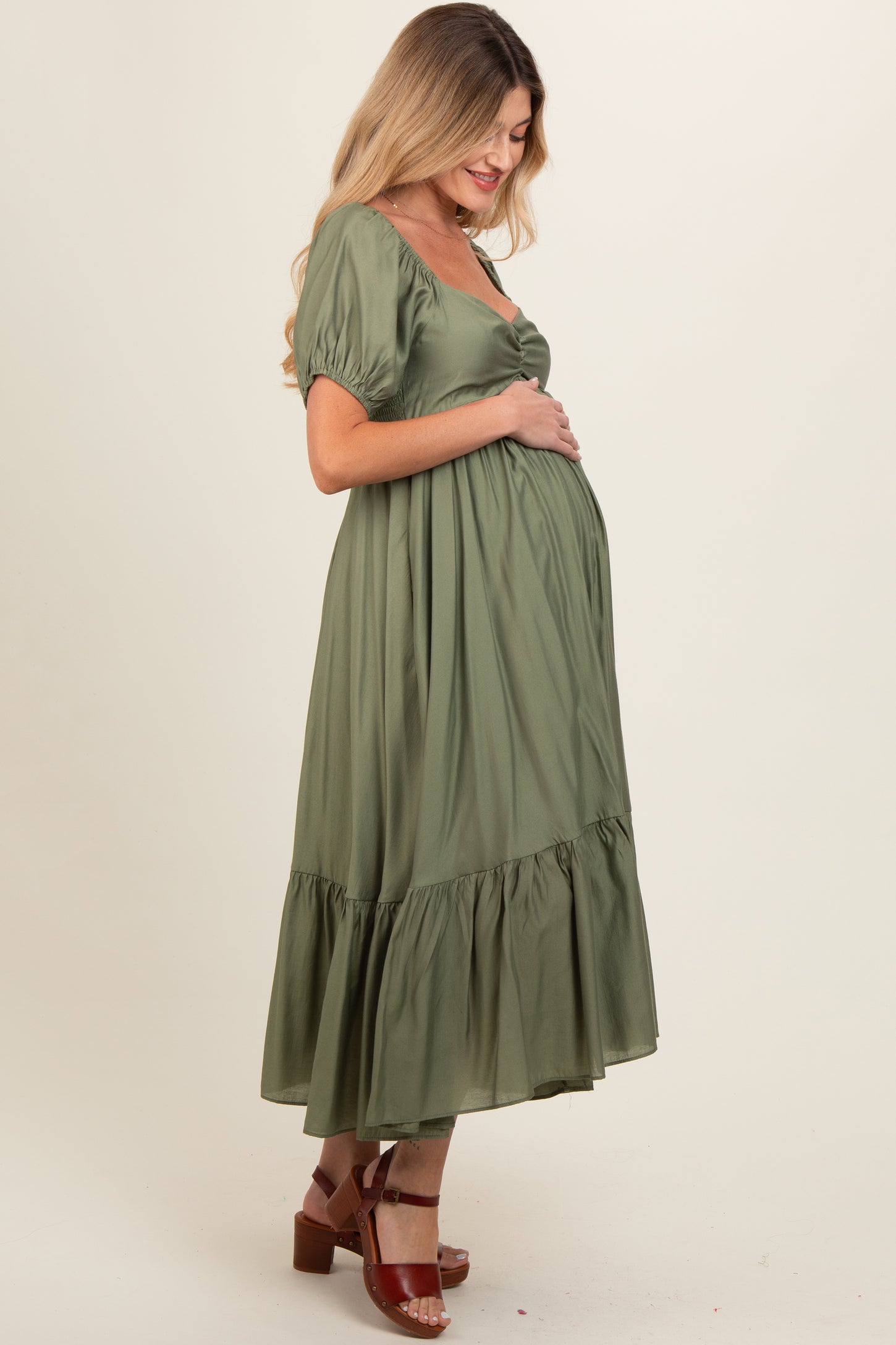 woman wearing an olive green maternity dress with short puff sleeves and a tiered skirt, holding her baby bump