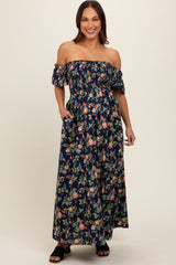 woman wearing a navy floral off-shoulder maternity maxi dress with pockets and a fitted bodice, displaying a baby bump