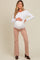 woman wearing a white long sleeve maternity top and beige flared maternity pants, showing her baby bump