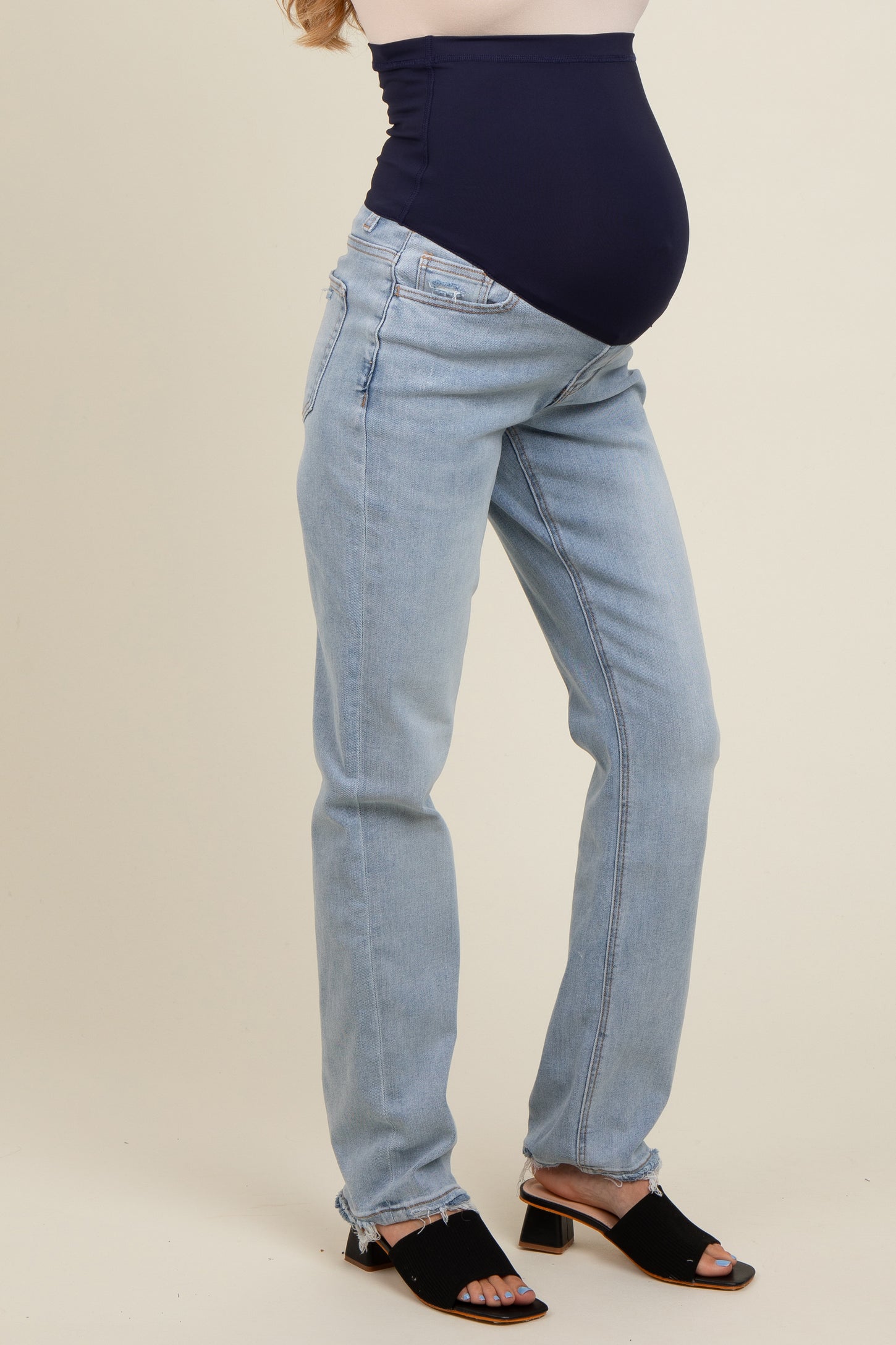 woman wearing light blue maternity jeans with a dark blue panel, showcasing a visible baby bump
