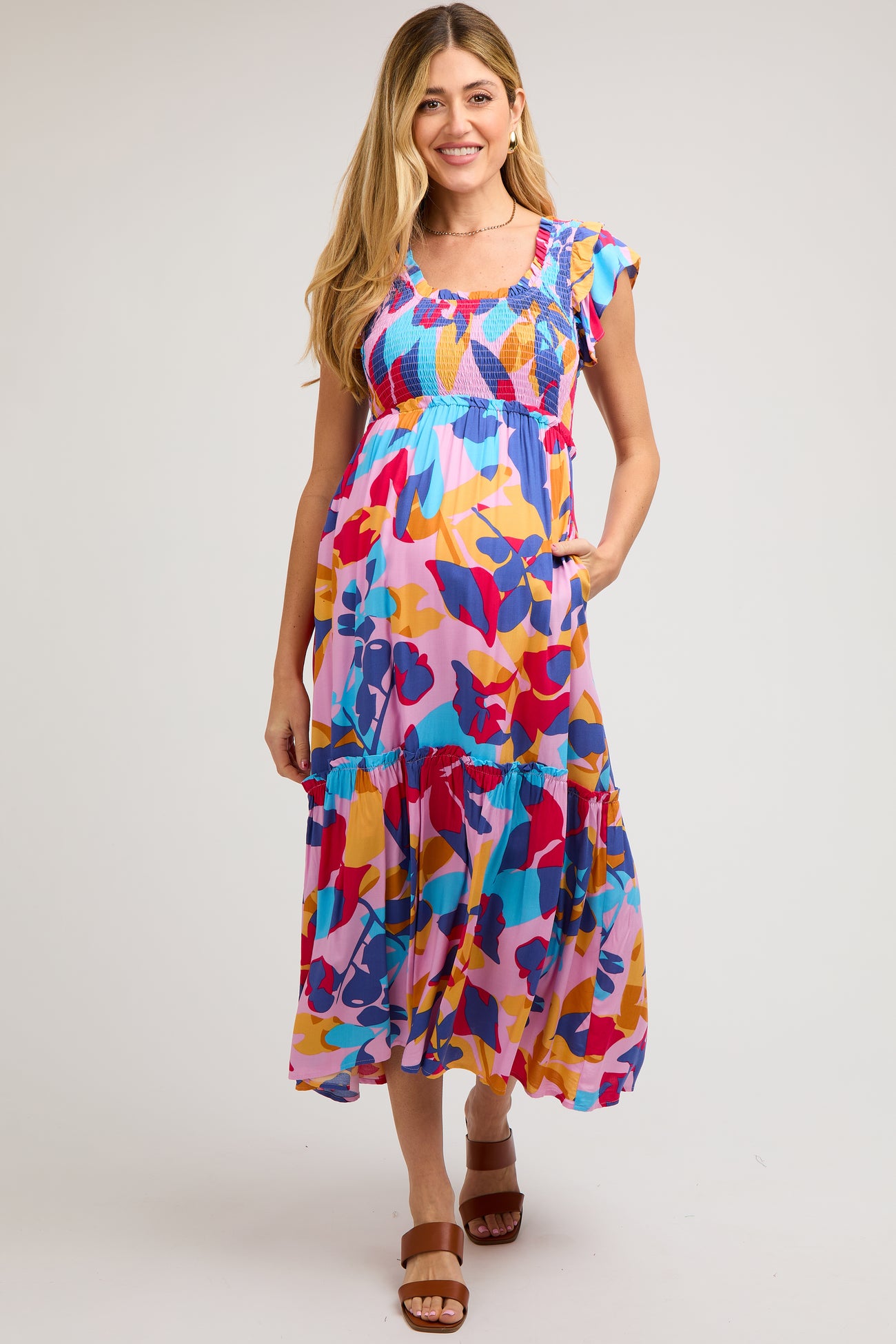woman wearing a colorful floral maternity dress with ruffled sleeves and tiered skirt, showing her baby bump