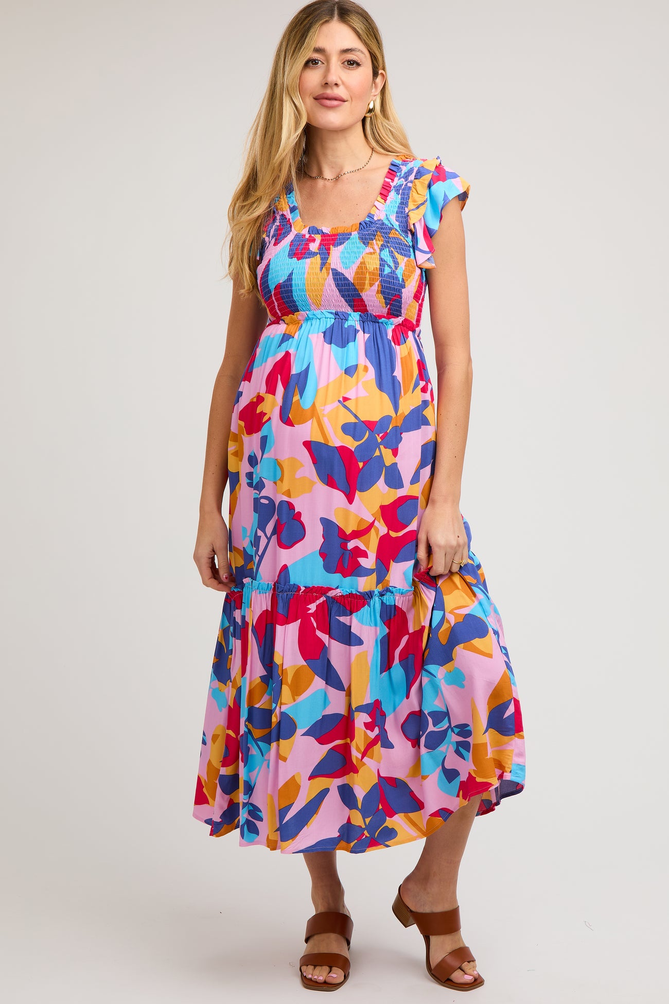 woman wearing a colorful floral maternity maxi dress with ruffle sleeves and a tiered skirt, showing her baby bump