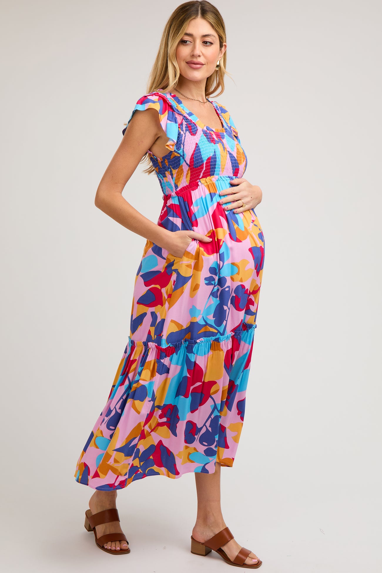 woman wearing a colorful floral maternity maxi dress with ruffled sleeves and side pockets, showing her baby bump