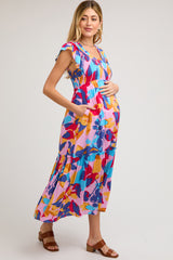 woman wearing a colorful floral maternity maxi dress with ruffled sleeves and side pockets, showing her baby bump