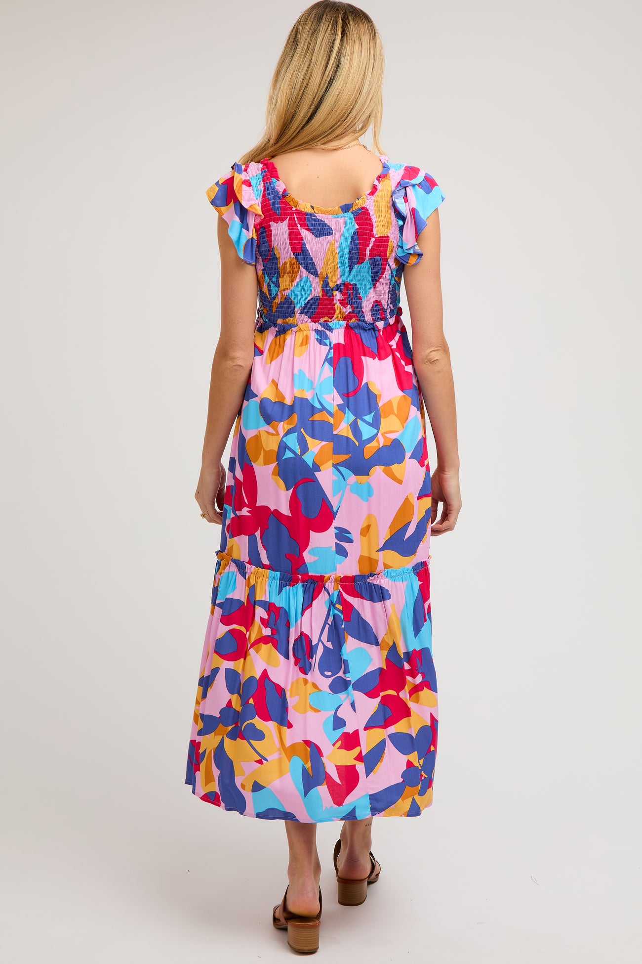 woman wearing a colorful floral maternity maxi dress with ruffle sleeves and a tiered hem, showing her back
