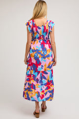woman wearing a colorful floral maternity maxi dress with ruffle sleeves and a tiered hem, showing her back