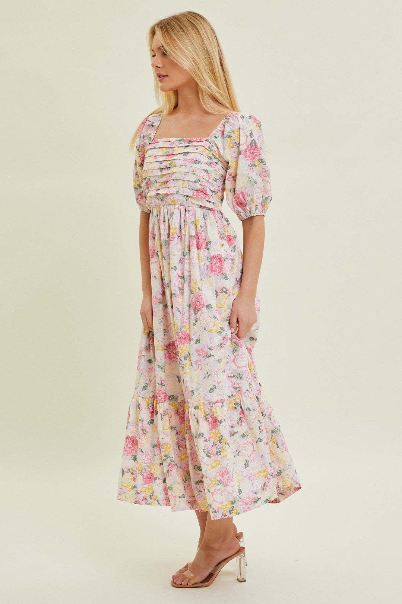 woman wearing a floral midi dress with square neckline and puff sleeves, standing in profile against a light background