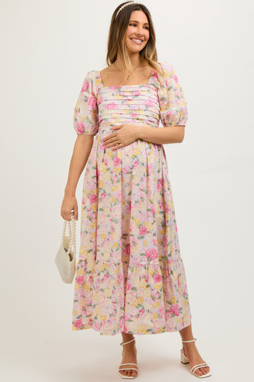 woman wearing a pink floral maternity dress with puff sleeves and a tiered skirt, holding her baby bump