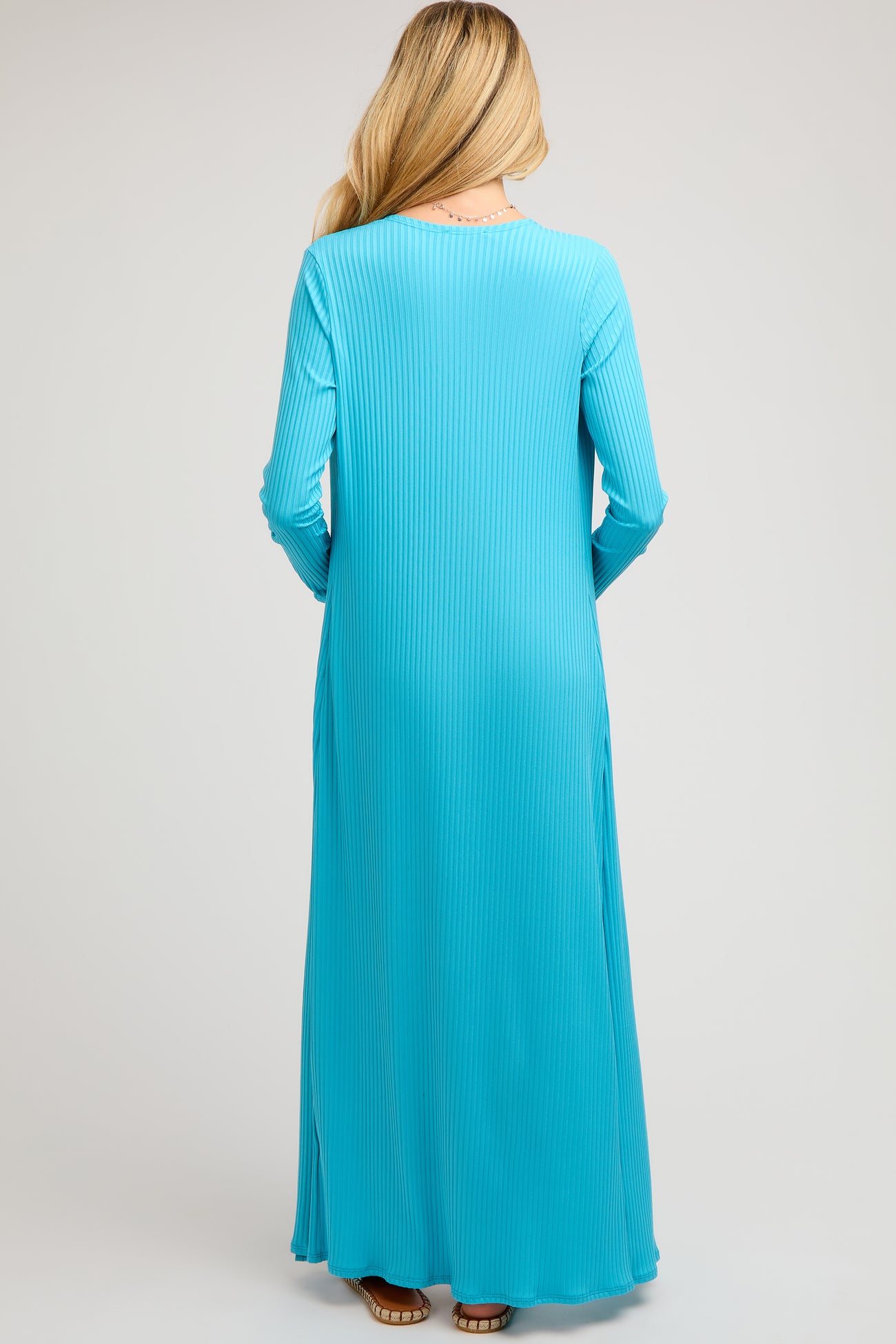 woman wearing a long sleeve turquoise maternity dress, shown from the back, highlighting the ribbed texture and full length