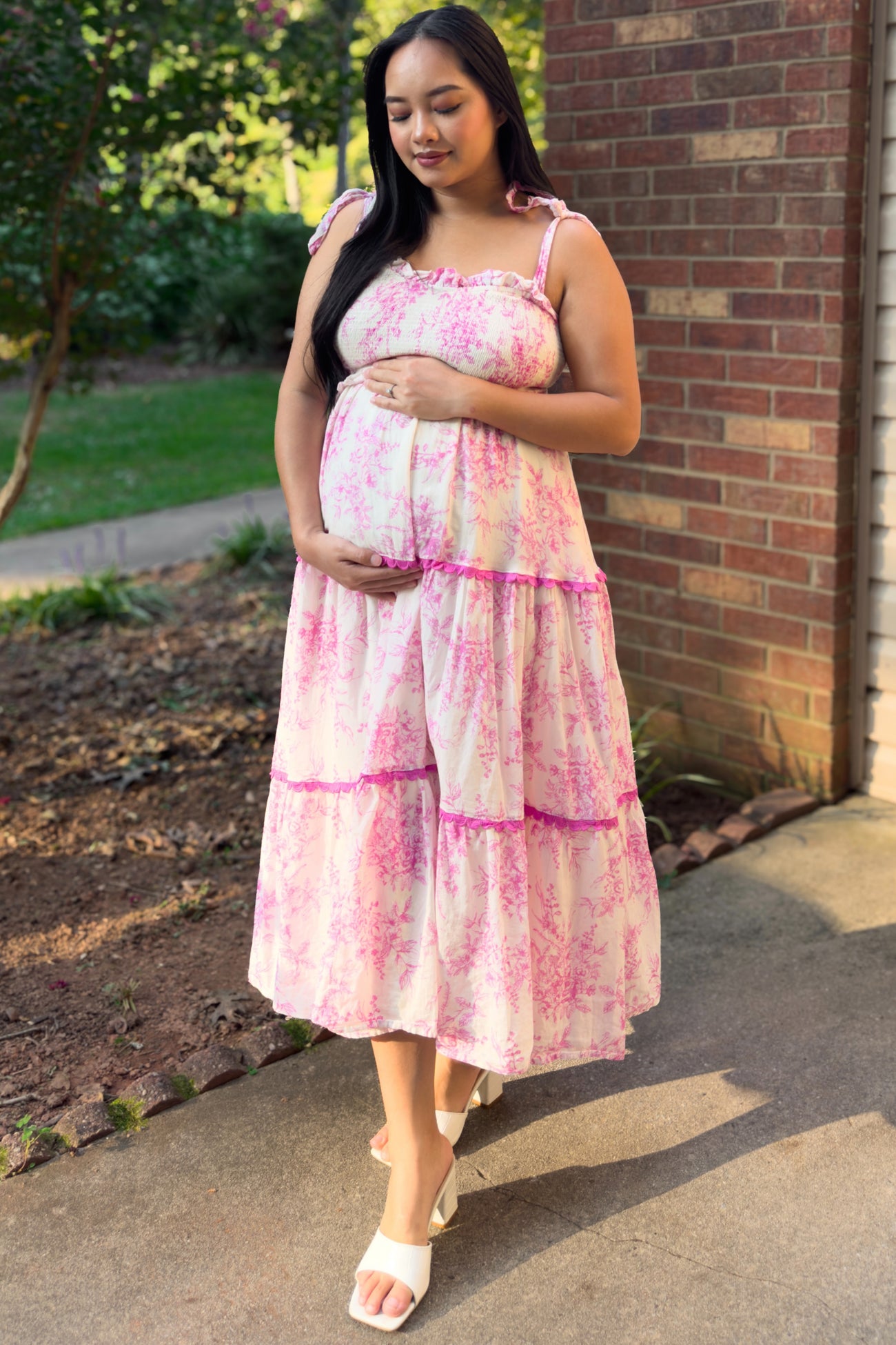 woman wearing a pink floral maternity dress with ruffle straps and holding her baby bump