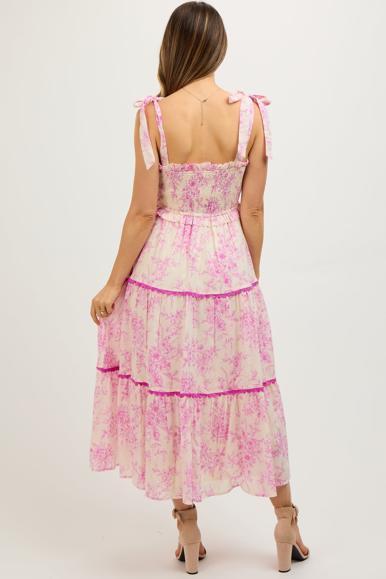 woman wearing a pink floral maternity maxi dress with tie straps and a tiered design, showing her baby bump