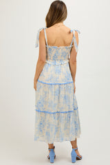 woman wearing a blue and cream floral print maternity dress with tie straps and tiered skirt, showing a baby bump
